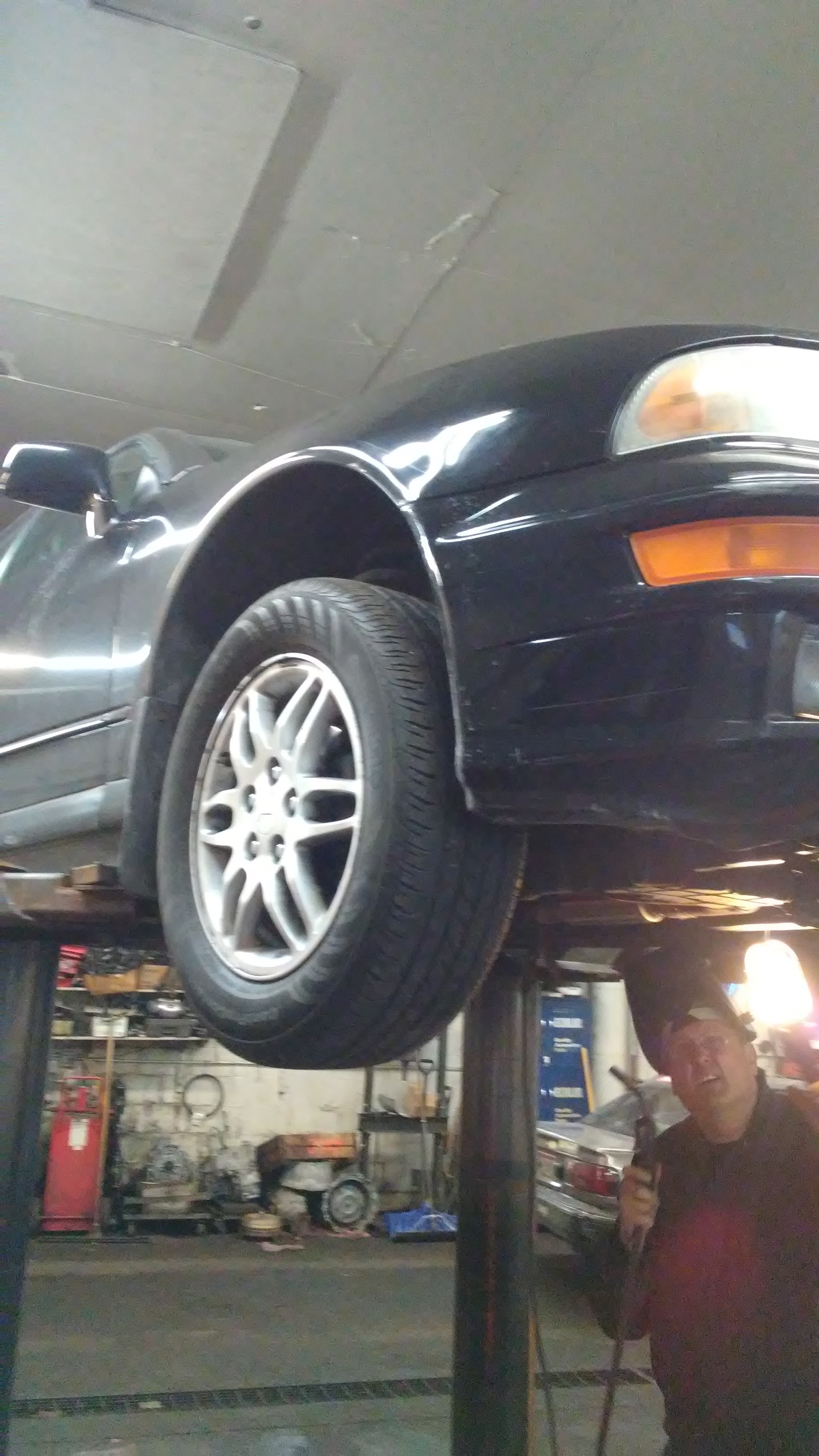 A black sedan raised on a two-post lift inside the Remington shop, a mechanic below holding a work light